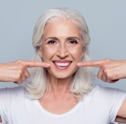 Woman pointing to her smile after full mouth reconstruction