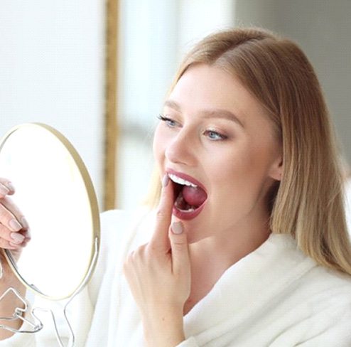 Young woman looking at her teeth in mirror