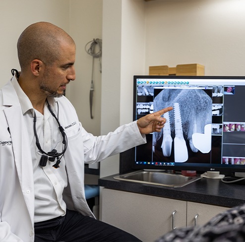 Doctor Villescas pointing to a computer screen showing an x ray of a patient with a dental implant