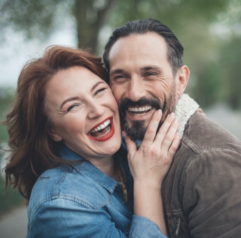 Man and woman smiling and holding each other outdoors