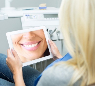 Woman looking at close up of smile on tablet screen in dental chair