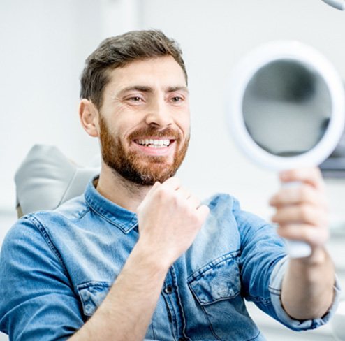 man smiling in mirror after smile makeover in Port Charlotte    