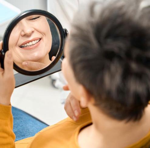 Dental patient using mirror to admire the results of her full mouth reconstruction treatmentTooth model sitting in front of calculator