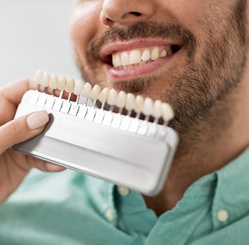 a dentist holding up a shade chart to a patient’s teeth