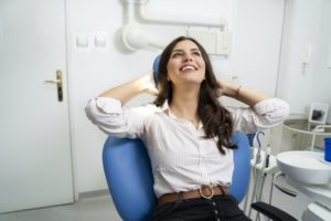 Woman relaxing in dental chair with hands behind head