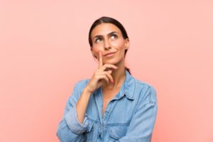 Woman thinking with hand on chin and pink background