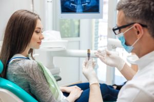 a dentist showing a patient an example of a dental implant