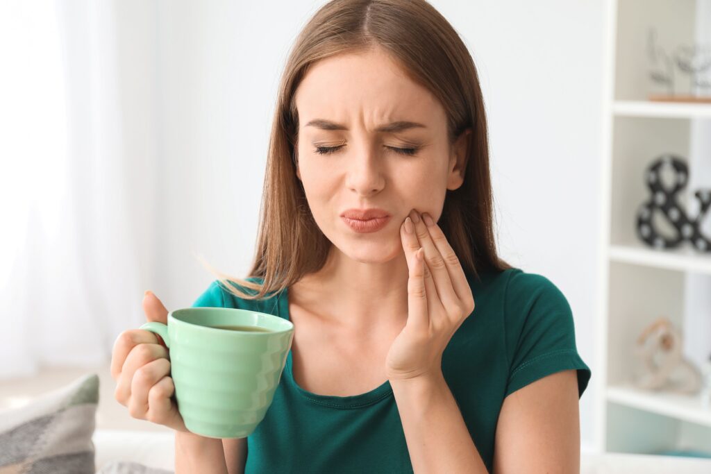 Woman holding cup of coffee touching jaw squinting in pain