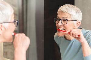 Senior woman with glasses brushing her teeth