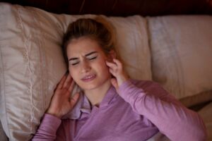 Woman lying in bed holding jaws in pain from bruxism.
